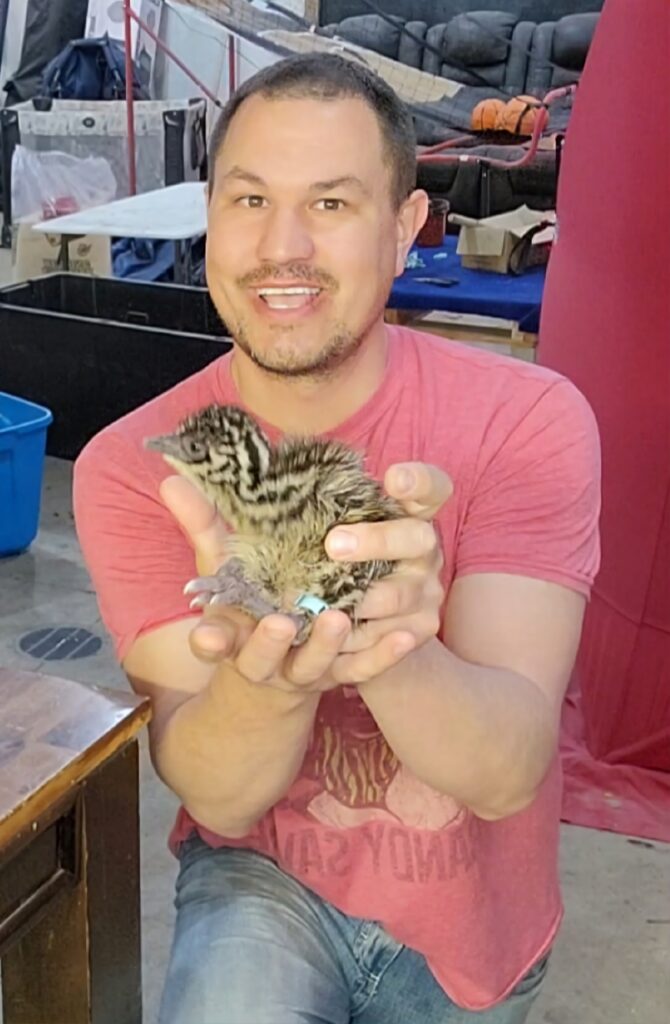 Cory Hinkel smiles while holding an emu chick.